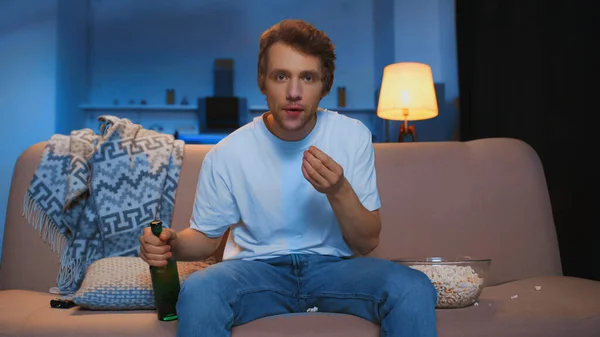 Tensed Young Man Bottle Beer Sitting Couch Bowl Popcorn While Royaltyfria Stockfoton