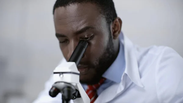 Concentrated african american scientist looking through microscope in clinical laboratory — Stock Photo