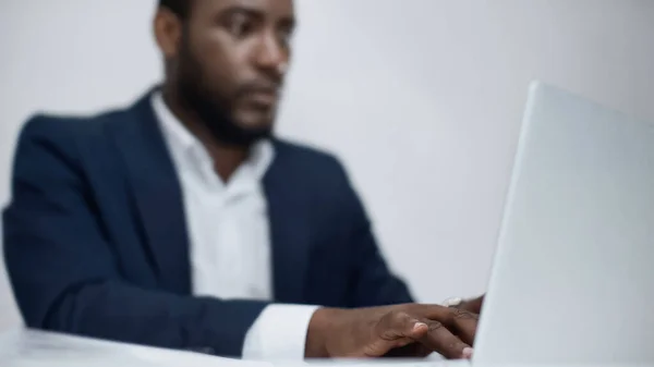 Blurred african american businessman using laptop isolated on grey — Stock Photo