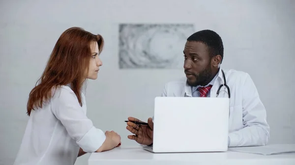 Médecin afro-américain parlant avec un patient roux à l'hôpital — Photo de stock