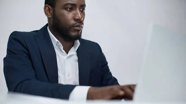 Uomo d'affari afroamericano utilizzando computer portatile offuscato isolato su grigio — Foto stock