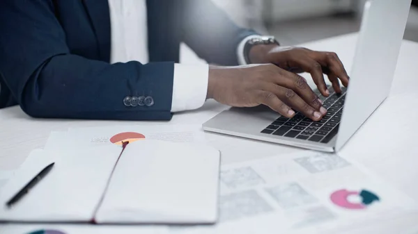 Teilansicht eines afrikanisch-amerikanischen Geschäftsmannes mit Laptop in der Nähe von Diagrammen auf dem Schreibtisch — Stockfoto