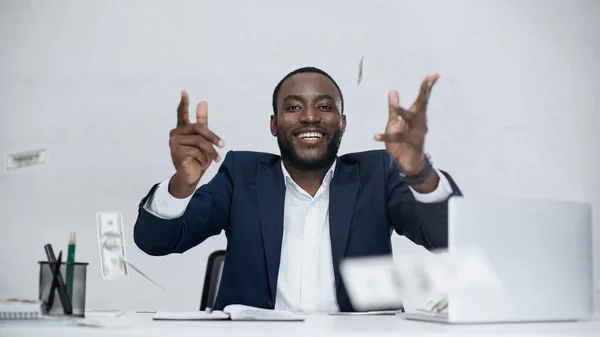 Joyeux homme d'affaires afro-américain jetant des billets en dollars dans l'air et souriant sur gris — Photo de stock