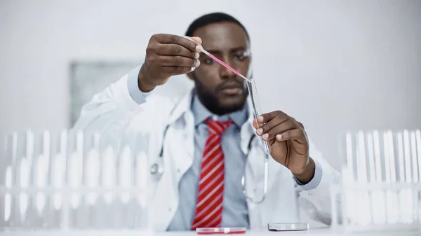 Verschwommener afrikanisch-amerikanischer Arzt fügt rote Flüssigkeit ins Reagenzglas — Stockfoto