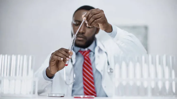 Verschwommener afrikanisch-amerikanischer Wissenschaftler fügt rote Flüssigkeit im Reagenzglas im Labor hinzu — Stockfoto