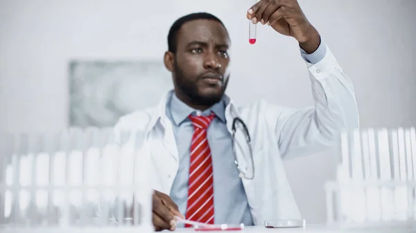 Bearded african american scientist looking at red liquid in test tube — Stock Photo