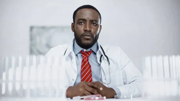 African american scientist sitting near blurred test tubes in laboratory — Stock Photo