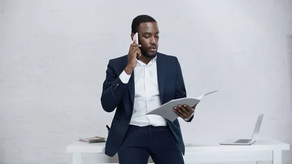 Serio uomo d'affari afroamericano che parla su smartphone mentre è in piedi con la cartella — Foto stock