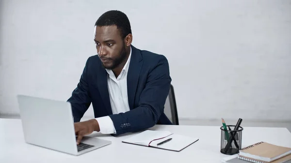 Hombre de negocios afroamericano serio escribiendo en el ordenador portátil en gris - foto de stock