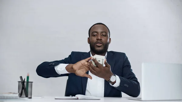 Rico hombre de negocios afroamericano sosteniendo billetes de dólar aislados en gris - foto de stock