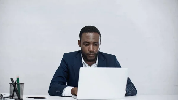 Hombre de negocios afroamericano utilizando portátil aislado en gris - foto de stock