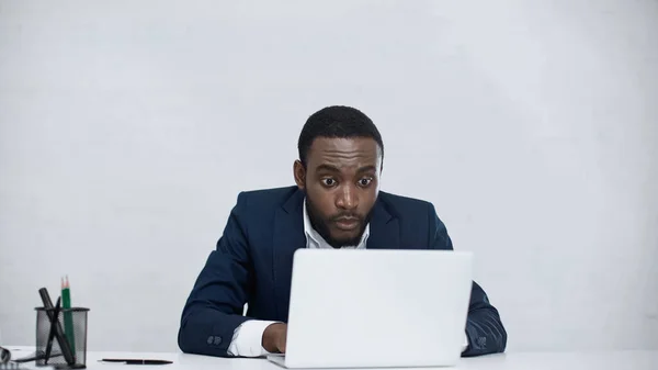 Shocked african american businessman using laptop isolated on grey — Stock Photo