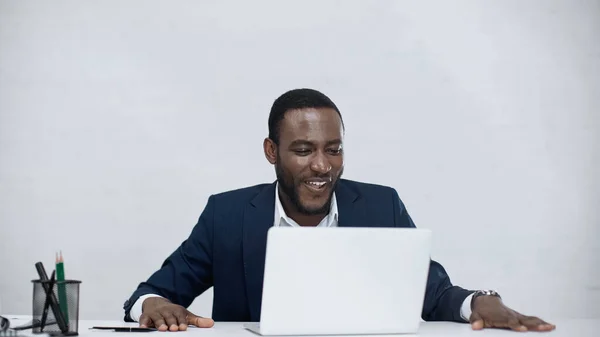 Empresário afro-americano alegre usando laptop isolado em cinza — Fotografia de Stock