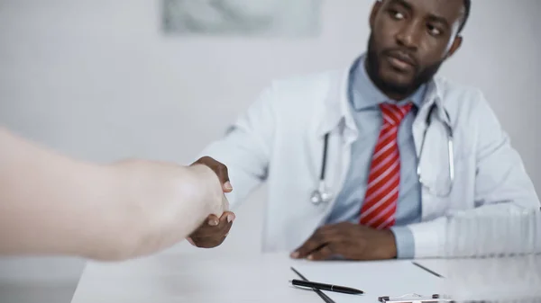 Médico afroamericano estrechando la mano con el paciente - foto de stock