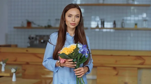 Hübsche Frau hält Blumenstrauß in der Hand und schaut zu Hause in die Kamera — Stockfoto