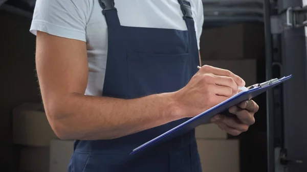 Cropped view of delivery man writing on clipboard outdoors — Stock Photo