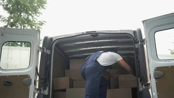 Доставщик в форме забирает коробку из машины на открытом воздухе — стоковое фото