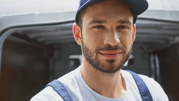 Delivery man in uniform looking at camera near blurred car outdoors — Stock Photo