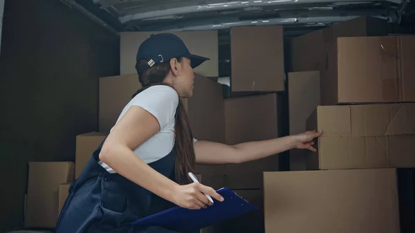 Delivery woman with clipboard standing near carton boxes in car — Stock Photo