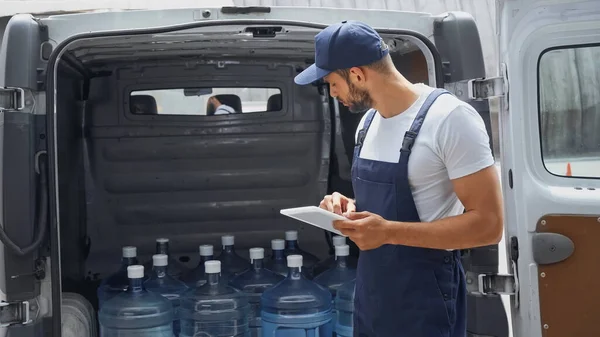 Side view of courier using digital tablet near bottles in car outdoors — Stock Photo