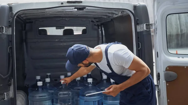 Mensajero sosteniendo tableta digital cerca de botellas en el coche al aire libre - foto de stock