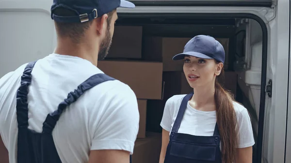 Delivery woman in uniform looking at colleague near boxes in car outdoors — Stock Photo