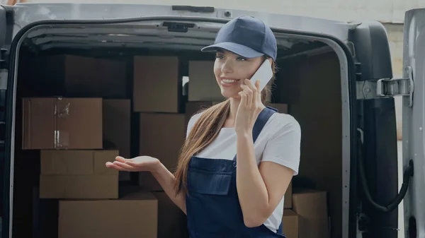 Positive courier talking on cellphone near carton boxes in auto outdoors — Stock Photo