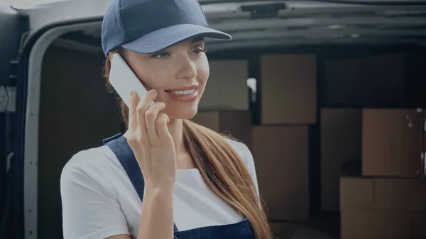 Mulher de entrega positiva falando no telefone celular perto de pacotes borrados no carro ao ar livre — Fotografia de Stock