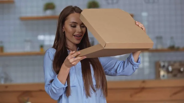 Улыбающаяся брюнетка смотрит на коробку для пиццы дома — стоковое фото