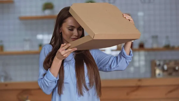 Mujer morena oliendo la caja de pizza abierta en casa - foto de stock