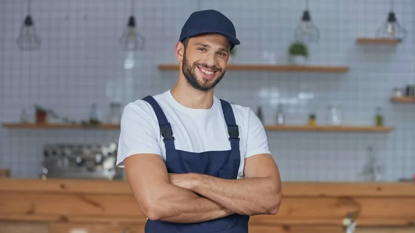 Gut gelaunter Kurier in Uniform und Mütze blickt zu Hause in die Kamera — Stockfoto