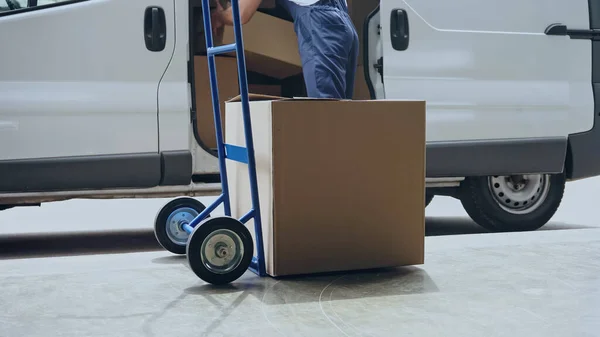 Vue recadrée du livreur prenant la boîte en carton de la voiture près du chariot à l'extérieur — Photo de stock