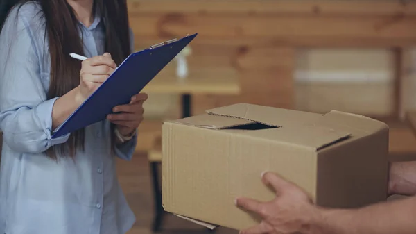 Vue recadrée du courrier tenant la boîte de carton près de la femme écrivant sur le presse-papiers à la maison — Photo de stock