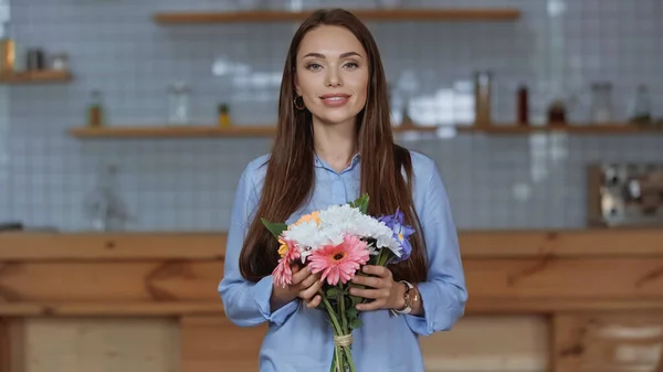 Fröhliche Frau mit Blumenstrauß und Blick in die Kamera zu Hause — Stockfoto