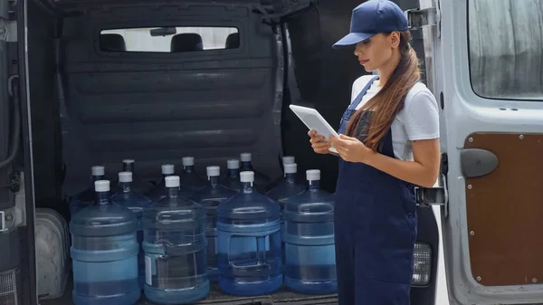 Brunette livraison femme utilisant tablette numérique près de bouteilles avec de l'eau en voiture à l'extérieur — Photo de stock