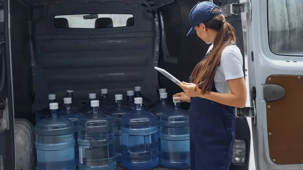 Курьер держит цифровой планшет возле пластиковых бутылок в автомобиле на открытом воздухе — стоковое фото