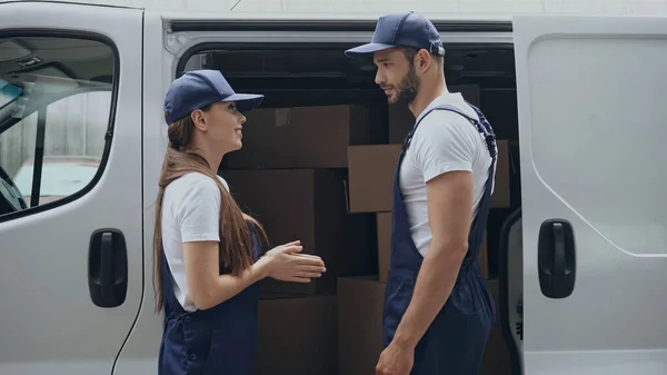 Side view of smiling courier talking to colleague near car outdoors — Stock Photo