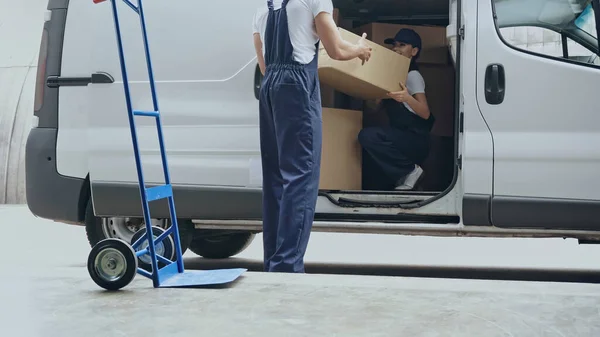 Smiling delivery woman in car holding carton box near colleague outdoors — Stock Photo