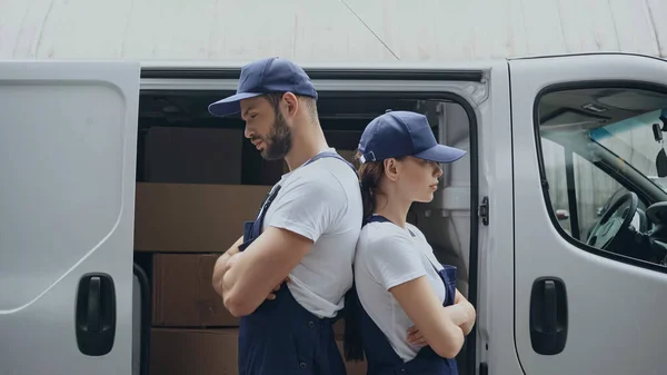 Side view of couriers standing back to back near car with carton boxes outdoors — Stock Photo