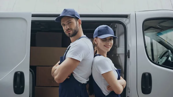 Couriers in uniform standing back to back near carton boxes outdoors — Stock Photo