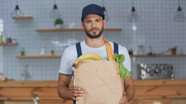 Delivery man looking at camera while holding package with food at home — Stock Photo