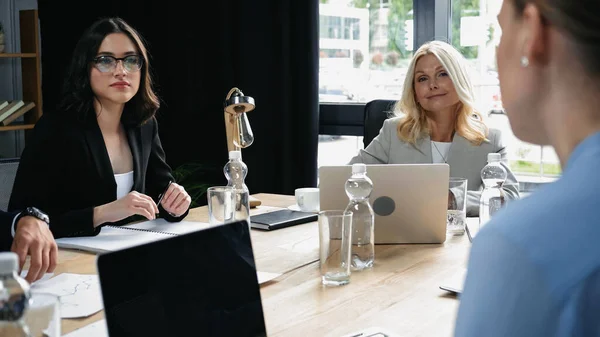 Geschäftsfrau mittleren Alters lächelt neben Laptop und jungen Kollegen im Besprechungsraum — Stockfoto