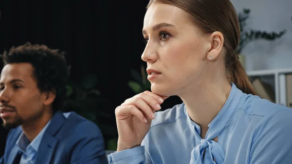 Young businesswoman thinking near blurred african american colleague in office — Stock Photo