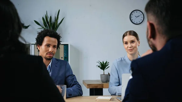 Back view of blurred business people near interracial colleagues in meeting room — Stock Photo