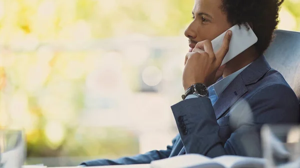 Seitenansicht eines jungen afrikanisch-amerikanischen Geschäftsmannes, der im Büro mit dem Handy spricht — Stockfoto