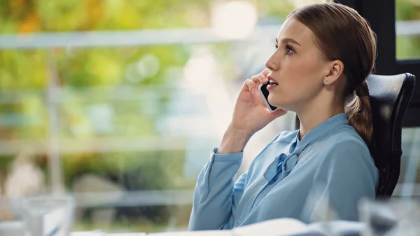 Vista lateral de la joven empresaria hablando en el teléfono inteligente en la oficina - foto de stock