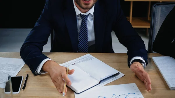 Vista ritagliata di uomo d'affari in abbigliamento formale gesticolando vicino notebook vuoto e documenti — Foto stock