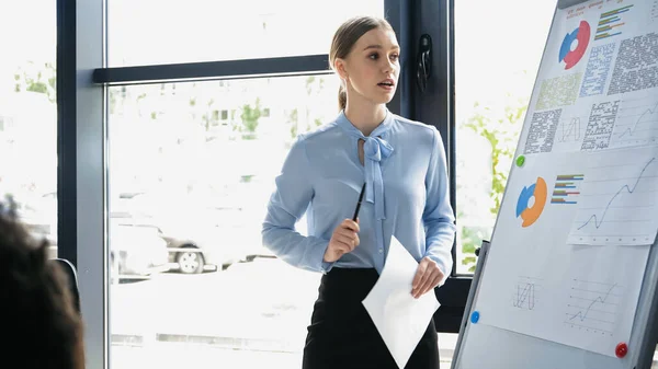 Young businesswoman looking at flip chart with graphs in office — Stock Photo