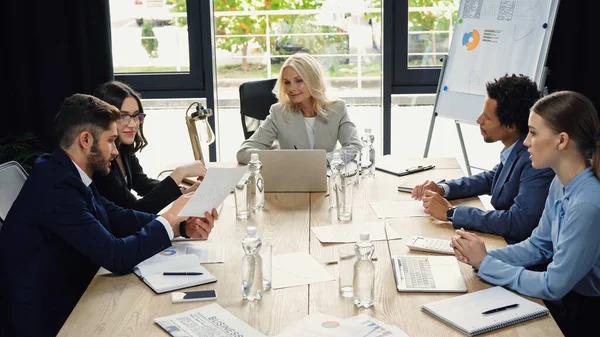 Junger Geschäftsmann hält Dokument während eines Treffens mit multiethnischen Kollegen — Stockfoto