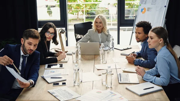 Young manager pointing at document near interracial business people in meeting room — Stock Photo